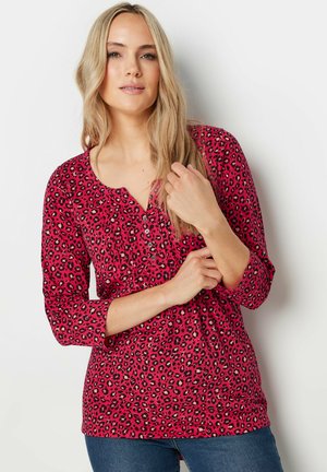 Haut en imprimé léopard fuchsia avec un col rond, des manches trois-quarts et des détails en boutons. Tissu doux avec une coupe décontractée.