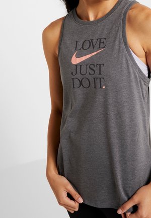 Kobieta ubrana w szary top bez rękawów z napisami „LOVE” i „JUST DO IT” oraz różowym logo Nike Swoosh z przodu.