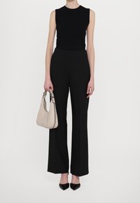 Sort ærmeløs top med ribbet tekstur, højtaljede sorte vide bukser og en blød beige håndtaske med justerbar rem. Sorte spidse heels.