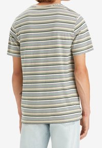 T-shirt à manches courtes rayé en beige, avec des rayures horizontales vertes et bleu marine. Tissu doux avec une coupe décontractée, col rond et coutures visibles.