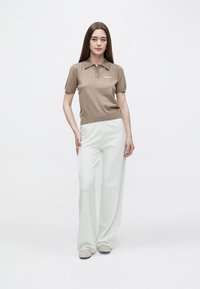 Rjava polo majica s kratkimi rokavi, ovratnikom in logotipom, kombinirana z belimi širokimi hlačami. Obleka ima mehko teksturo in sproščen kroj.