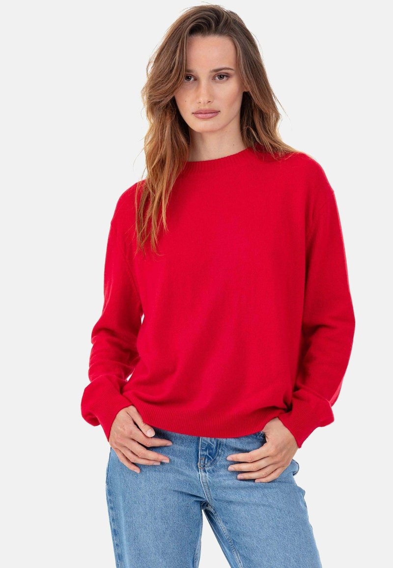 Pull en maille rouge avec un col rond et des manches longues ; texture douce ; porté par-dessus un jean en denim bleu clair.