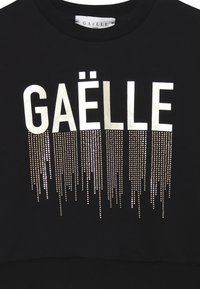 Felpa nera con la scritta "GÄËLLE" in bold lettere bianche, decorata con righe verticali di borchie metalliche per un tocco di dettaglio in più.