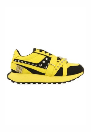 Baskets jaunes et noires avec semelle épaisse, clous métalliques et sangles avec pointes argentées sur le dessus et les côtés.