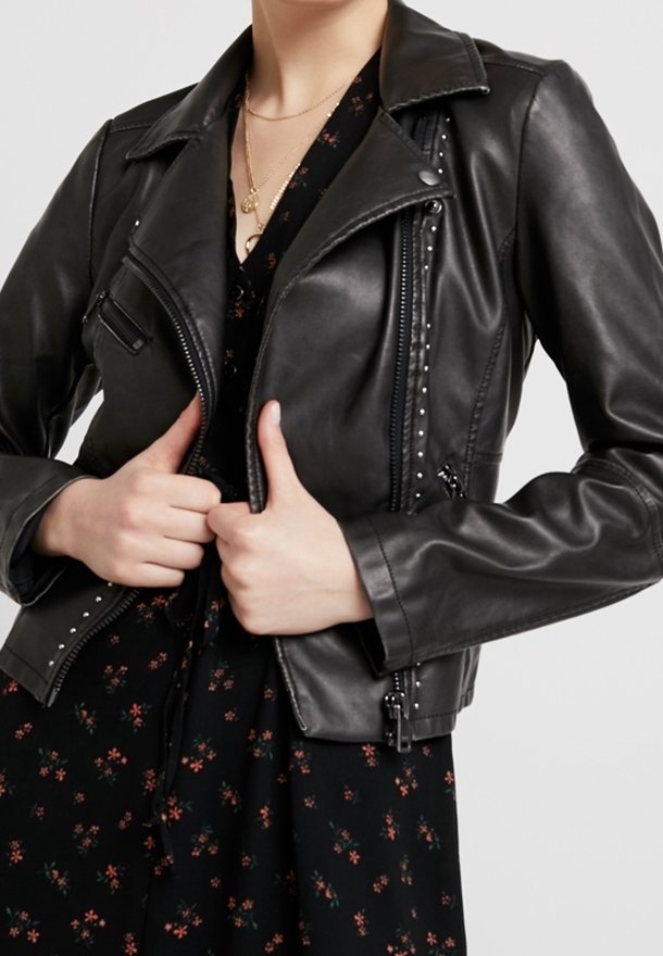 Giubbotto da motociclista in pelle nera con tasche con zip, dettagli borchiati e colletto a punte, indossato sopra un vestito floreale scuro.