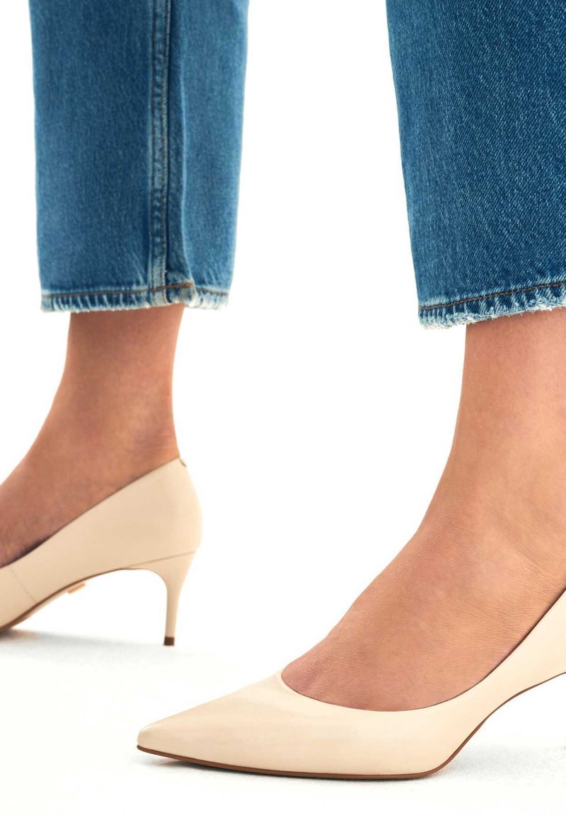 Escarpins beige à bout pointu avec un petit talon et une finition lisse. Portés avec un jean bleu court à ourlet brut. Design simple sans ornements.