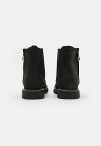 Botines negros de ante hasta el tobillo con cremalleras laterales, suelas de goma planas y un diseño sencillo. Presenta una punta redondeada y detalles de costura mínimos.