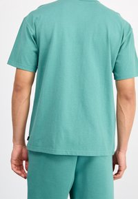 Turkusowa bawełniana koszulka z krótkim rękawem i luźnym krojem. Bezszwowy dekolt i mała metka z logo blisko dołu. Miękka, gładka tekstura.