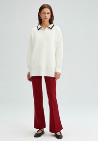 Oversized wit sweater met een zwart omzoomde kraag, gecombineerd met rode flare broeken en zwarte schoenen. Glad textuur, losse pasvorm.
