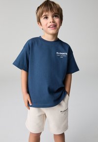 Granatowy bawełniany t-shirt z krótkimi rękawami i bia łym nadrukiem logo, zestawiony z beżowymi szortami z subtelnym logo na krawędzi.