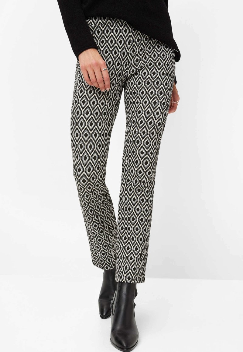 Pantalon à motifs noir et blanc avec un design en losange, coupe fuselée et tissu texturé. Associé à des bottines noires élégantes.