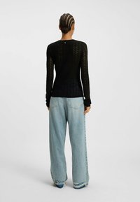 Haut noir texturé à manches longues avec une taille ajustée, associé à un jean bleu clair ample avec des ourlets déchirés et des poches visibles.