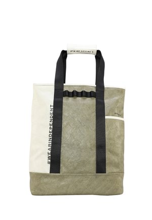 Tofarvet oliven- og hvid tote-taske med sorte håndtag, #WEARINDEPENDENT tekst og koordinater trykt på håndtagsomviklingen.