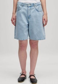 Lichtblauwe denim shorts met een relaxte pasvorm, vijf-pocket ontwerp, gebogen zoom en zichtbare stikdetails. Draagt met zwarte flats.