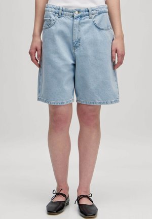 Lichtblauwe denim shorts met een relaxte pasvorm, vijf-pocket ontwerp, gebogen zoom en zichtbare stikdetails. Draagt met zwarte flats.
