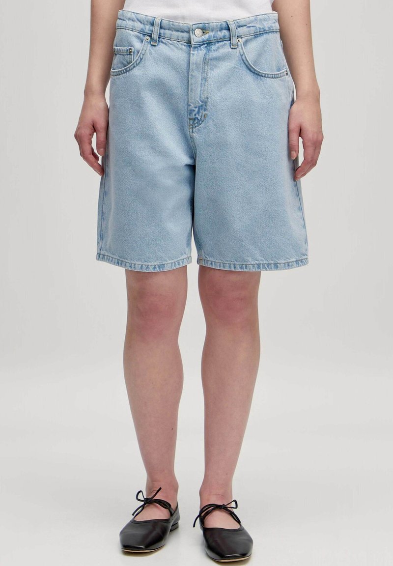 Lichtblauwe denim shorts met een relaxte pasvorm, vijf-pocket ontwerp, gebogen zoom en zichtbare stikdetails. Draagt met zwarte flats.