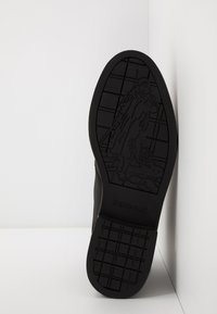 Semelle en caoutchouc noir avec motif de semelle et figure en relief ; conçue avec une finition lisse et le nom de la marque "Barbour" clairement visible sur le côté.