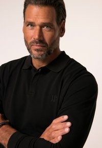 Schwarzes Poloshirt aus strukturiertem Stoff, mit einer Drei-Knopf-Leiste und einem dezenten gestickten Logo auf der Brust.