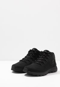 Schwarze Wanderschuhe aus strukturiertem Material mit abgerundeter Spitze, Schnürdesign und einem Logo an der Seite. Gummisohle für besseren Halt.