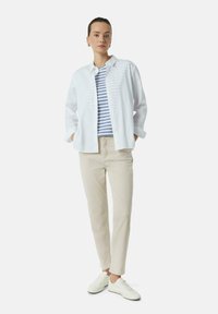 Weiße Hemdbluse über einem blau-weiß gestreiften T-Shirt, kombiniert mit beigen Hosen und weißen Sneakers. Einfaches, lässiges Outfit.