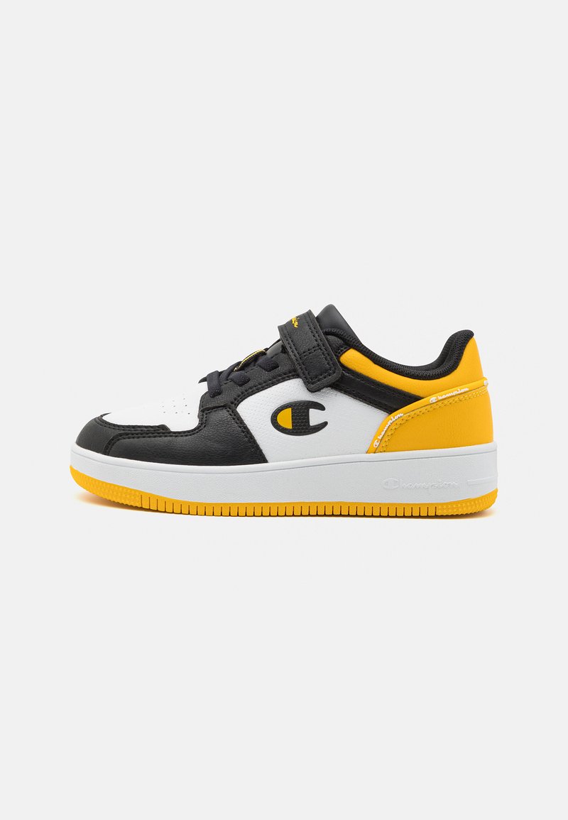 Svart, hvit og gul sporty sko med en glatt skinnoverdel, borrelåsstropp, gummisåle og logoakcent på siden.