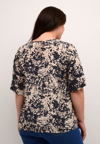 Blouse à imprimé floral en beige et marine, avec des manches courtes et un détail en trou de clé au dos. Tissu doux avec une coupe décontractée.