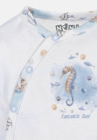 Korte mouwen babyshirt van witte katoen met lichtblauwe accenten en een zee-thema print, met een zeepaardje en kleine vissen. Blauwe drukknoopjes bij de hals.
