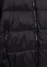 Geacă neagră tip puffer, cu secțiuni matlasate, material din nylon lucios și fermoar central cu un mâner negru pe partea stângă.