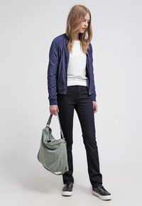 Marine bomberjakke over en hvit stripete genser, sammen med svarte jeans og mørke sneakers. En grønn semsket skulderveske henger fra armen.