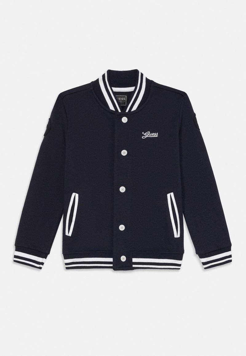 Veste varsity bleu marine avec col, poignets et poches à rayures blanches, boutons sur le devant et logo Guess sur la poitrine gauche.