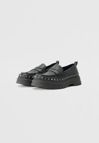 Svarta slip-on skor med en tjock plattform. Tillverkade av texturerat material, med ett dekorativt naglat band runt sulan. Detaljerad sömnad över vampen.