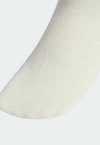 Detailný záber na bielu ponožku ukazujúci jemnú pletenú textúru a bezšvovú časť na prstoch na jednoduchom svetlom pozadí.