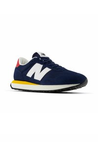 Zapatilla de deporte azul marino con logo blanco "N", acento rojo en el talón, entresuela amarilla y suela de goma negra. Presenta una combinación de materiales de malla y gamuza.