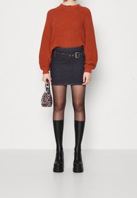 Maglione a coste in rust, mini gonna in denim scuro con dettagli in fibbia, collant neri trasparenti e stivali neri con tacco a ginocchio. Piccola borsa con stampa leopardata.