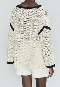 Pull en tricot crème avec une coupe ample, présentant des rayures noires sur les manches et le col, et une texture en maille ouverte et respirante.