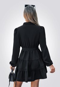 Černé šaty s několika vrstvami, dlouhé rukávy, pásek v pase a límečkem. Hladká tkanina s vrstveným volánkovým designem.