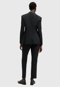 Svart skräddarsydd kavaj med strukturerade axlar, peplummidja och slim-fit svarta byxor. Har en stilren design och subtil textur.