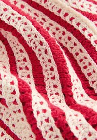 Tissu crocheté rouge et beige présentant des rayures alternées en plein et en ajour, mettant en valeur un design texturé et superposé.