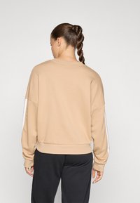 Beige genser med avslappet passform, rund hals og hvite sidestriper. Mykt stoff og ribbestrikkede mansjetter ved hem og ermer.
