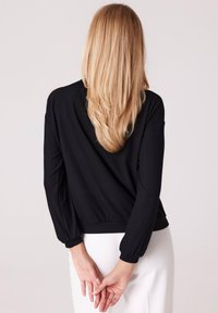 Czarny prążkowany sweter z długimi, lekko bufiastymi rękawami. Posiada dopasowany pas i dekolt w kształcie litery V na plecach. Gładka tekstura.