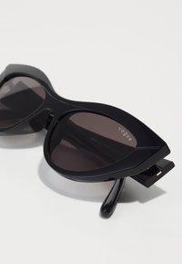 Ochelari negri de soare cu lentile întunecate în stil cat-eye. Prezintă un cadru din plastic lucios, colțuri proeminente și branding "vogue" pe partea superioară.