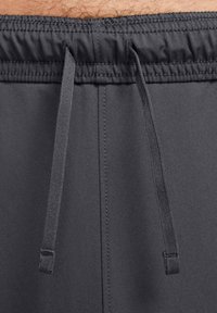 Harmaat urheilushortsit, joissa on joustava vyötärönauha ja kiristysnauhat. Sileä pinta, ei näkyviä kuvioita tai yksityiskohtia. Siisti muotoilu.