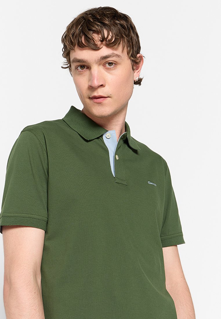 Polo vert à manches courtes, avec un col bleu clair et un petit logo sur le côté gauche. Fabriqué à partir d'un tissu doux avec une coupe classique.