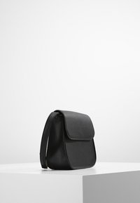 Černá kožená taška přes rameno zaobleného tvaru, s klopou a nastavitelným popruhem. Hladký povrch s minimalistickým designem.