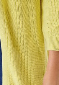 Pletený svetr v jasně žluté barvě. Obsahuje žebrovanou strukturu a široké rukávy. Měkký materiál s těsným manžetovým zakončením.
