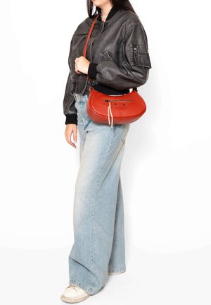 Rode leren handtas met een gebogen vorm en bovenrits, accentueert door een witte koordsluiting en contrasterende stiksels, gedragen als crossbody.