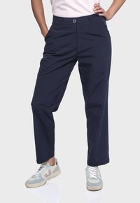 Marineblaue, leichte Hose mit geradem Schnitt, ausgestattet mit einem Knopfverschluss und seitlichen Taschen. Kombiniert mit grauen und pastellfarbenen Sneakers.