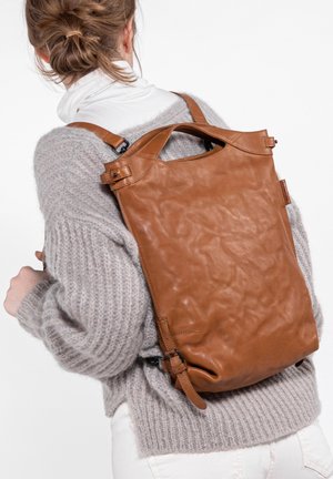 Brown leather backpack with a textured finish, roll-top closure, and adjustable straps, worn over a gray knitted sweater.