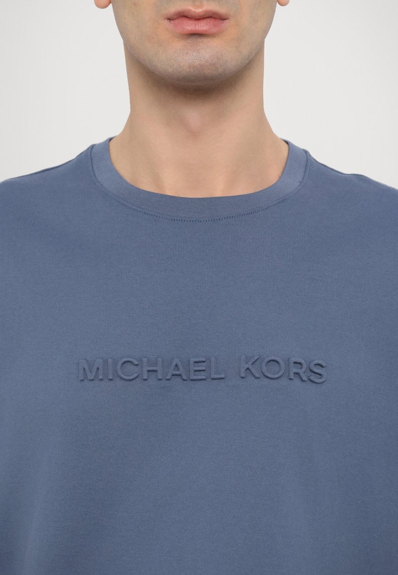 Blaues Baumwoll-T-Shirt mit Rundhalsausschnitt und erhabener Schriftzug "MICHAEL KORS" auf der Vorderseite. Glatte Textur und legere Gestaltung.