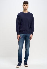 Námornícky pletený svetr s volným střihem, kombinovaný s úzkými modrými jeansy a námořnickými teniskami. Tento outfit má jednoduchý design a neformální texturu.